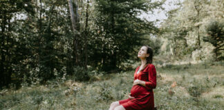 Pregnant woman in a red dress sitting in the woods
