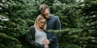 Pärchen mit Babybauch zwischen Tannenbäumen